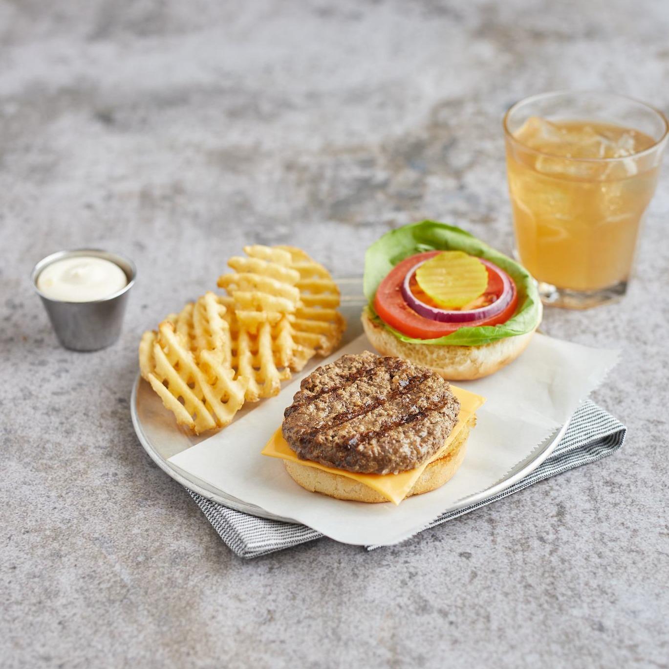AdvancePierre grilled beef patty on an open cheeseburger with vegetables, waffle fries and a drink