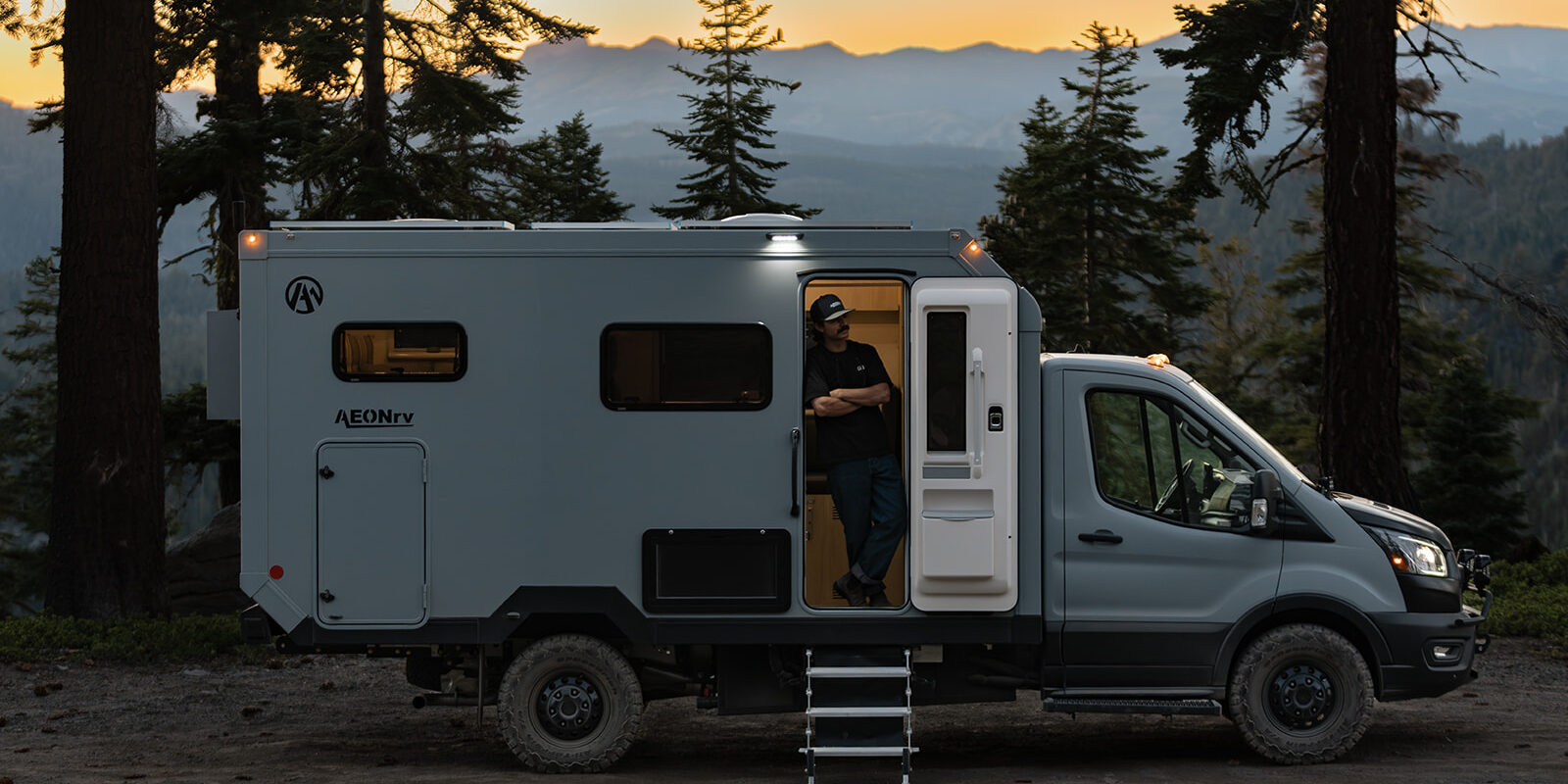 AEONrv camper parked among pines at sunset