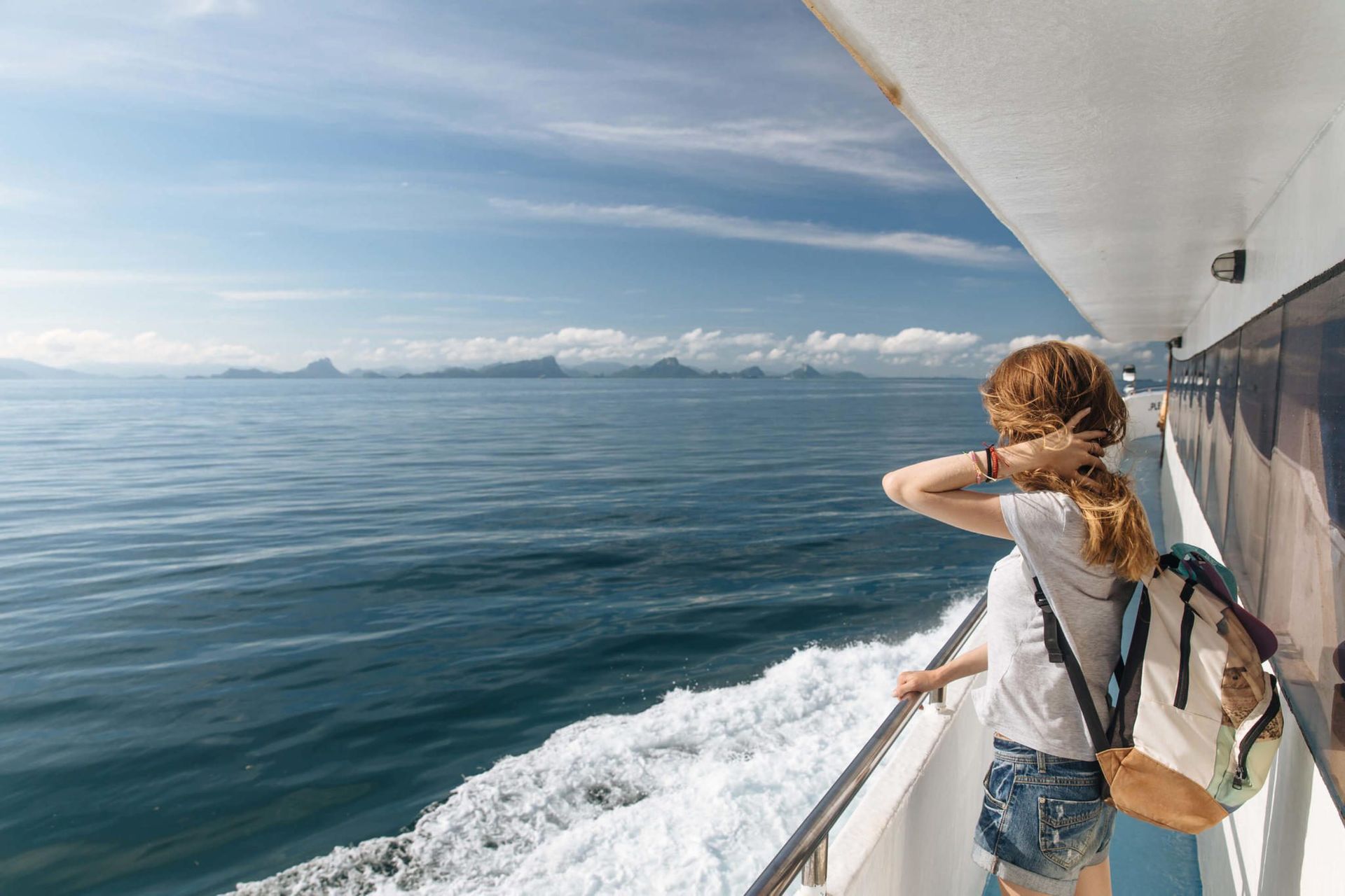A traveler with a backpack looking across the sea from a ferry