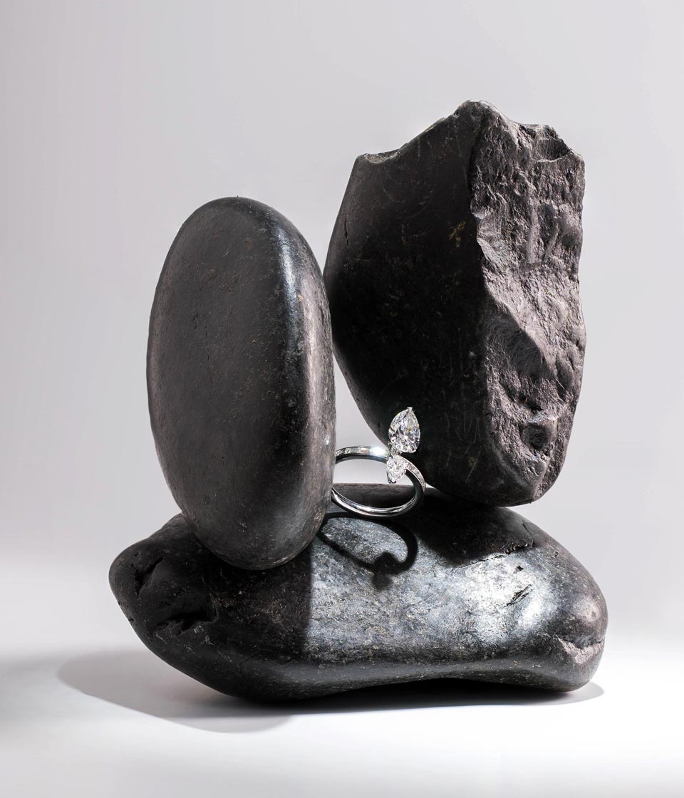 An open ring with two pear-shaped diamonds displayed among smooth and jagged dark rocks