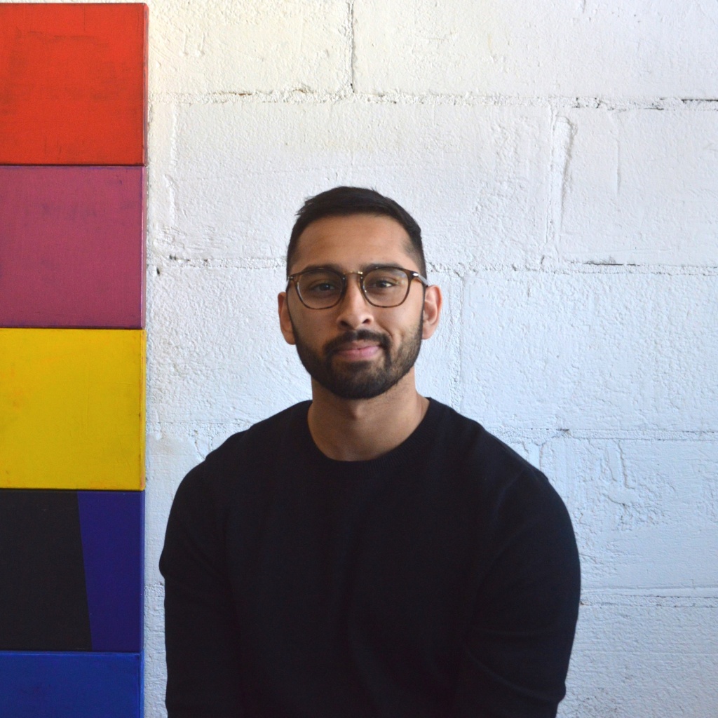 Afnan Rahman wearing glasses and a dark sweater, beside coloured wall panels