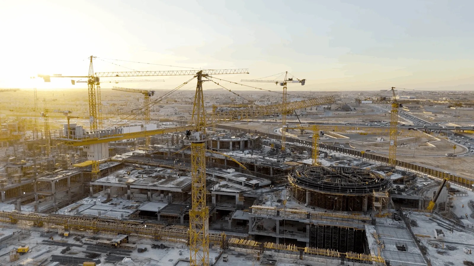 A large construction site at sunset with multiple tower cranes