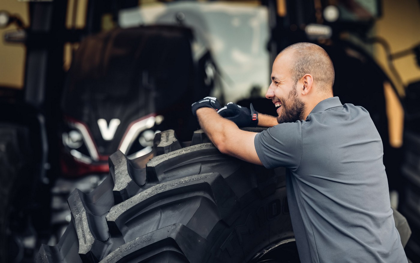 A technician leaning on a tire beside a Valtra tractor