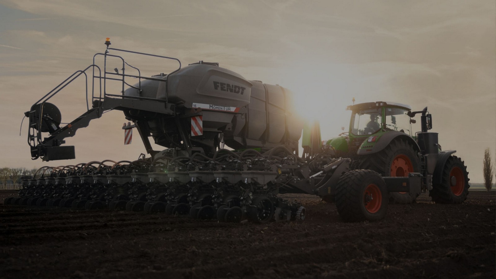 A Fendt tractor pulling a Momentum planter across a field at sunset
