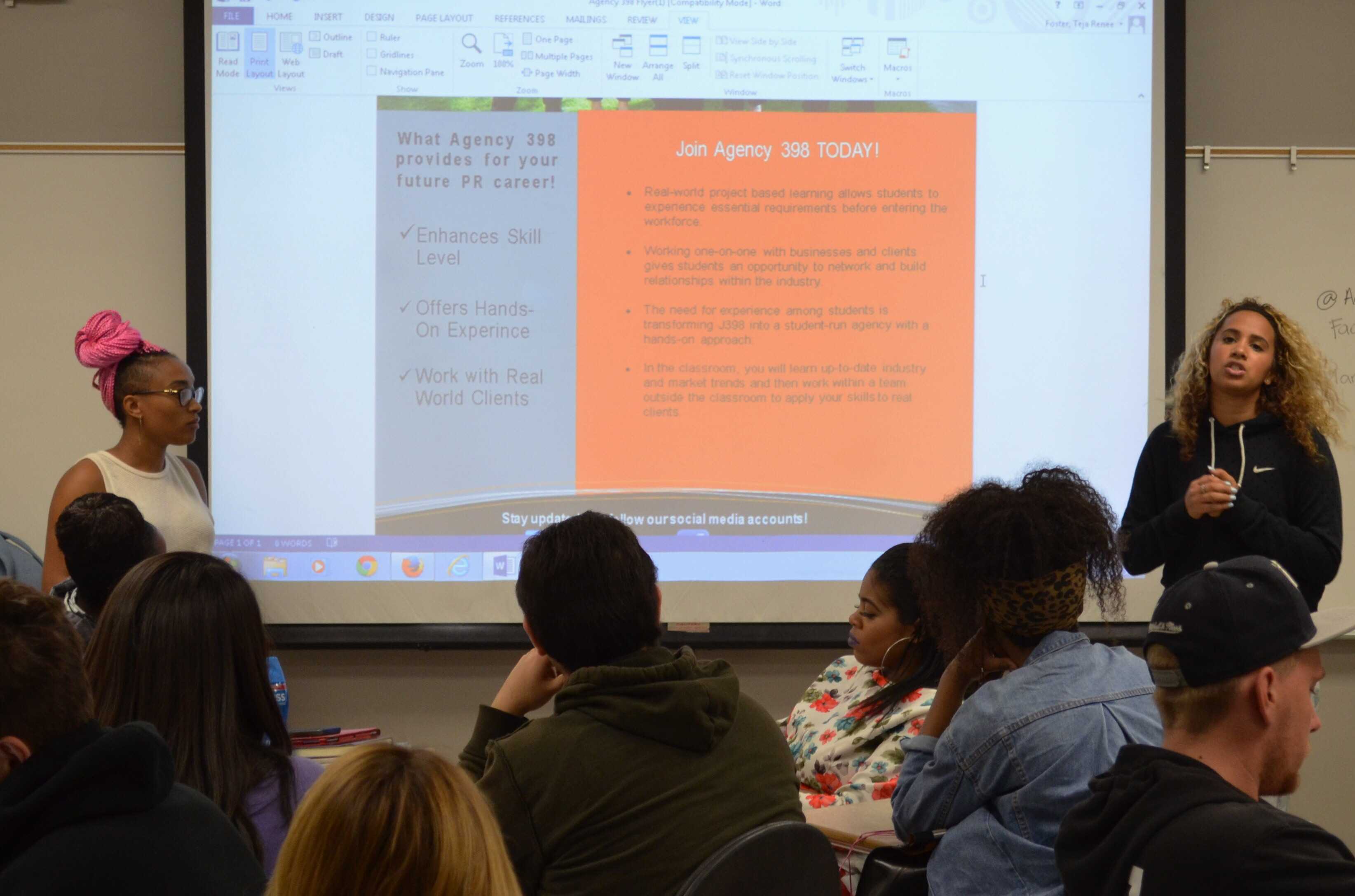 Agency 398 presenters speak to students beside a projected recruitment flyer in 2015