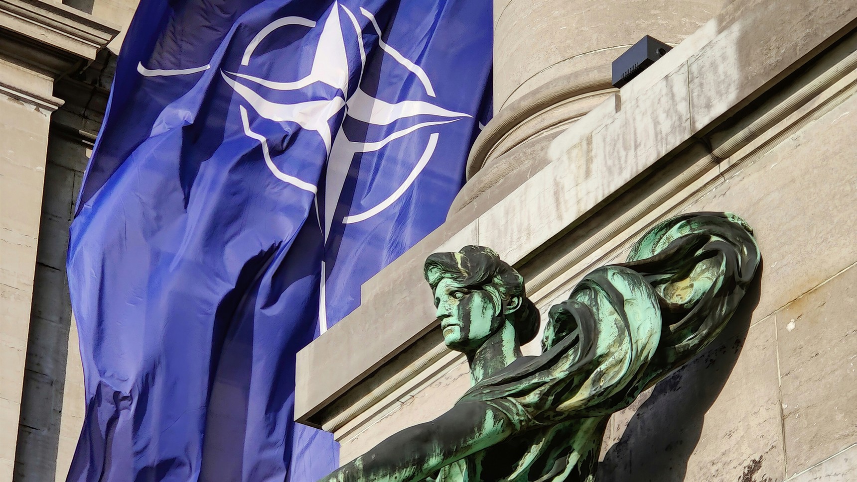 A NATO flag beside a stone figure at NATO headquarters