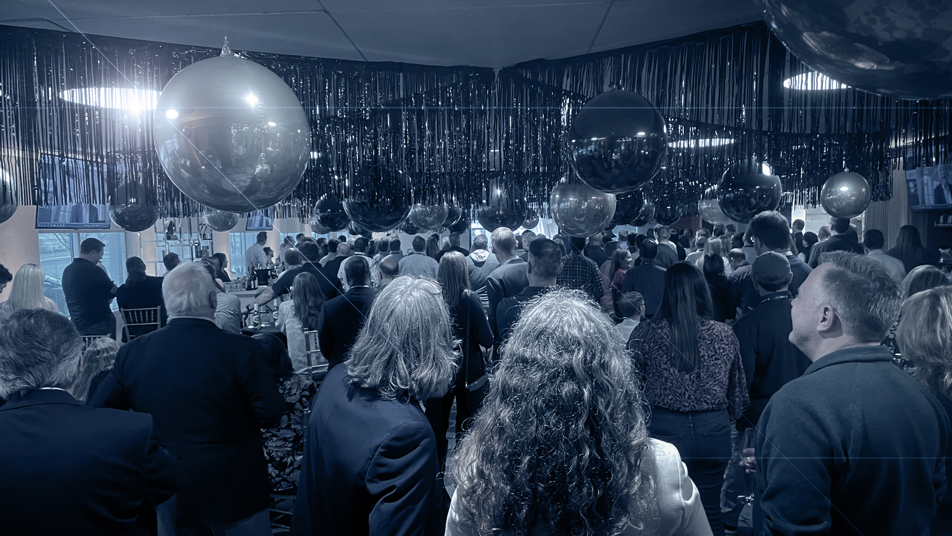People gathered beneath hanging silver spheres at an AGI company celebration