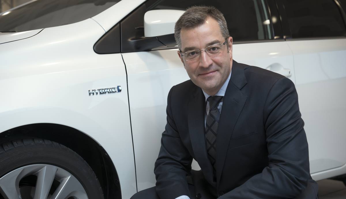 Agustin Martin crouching beside a white Toyota hybrid car