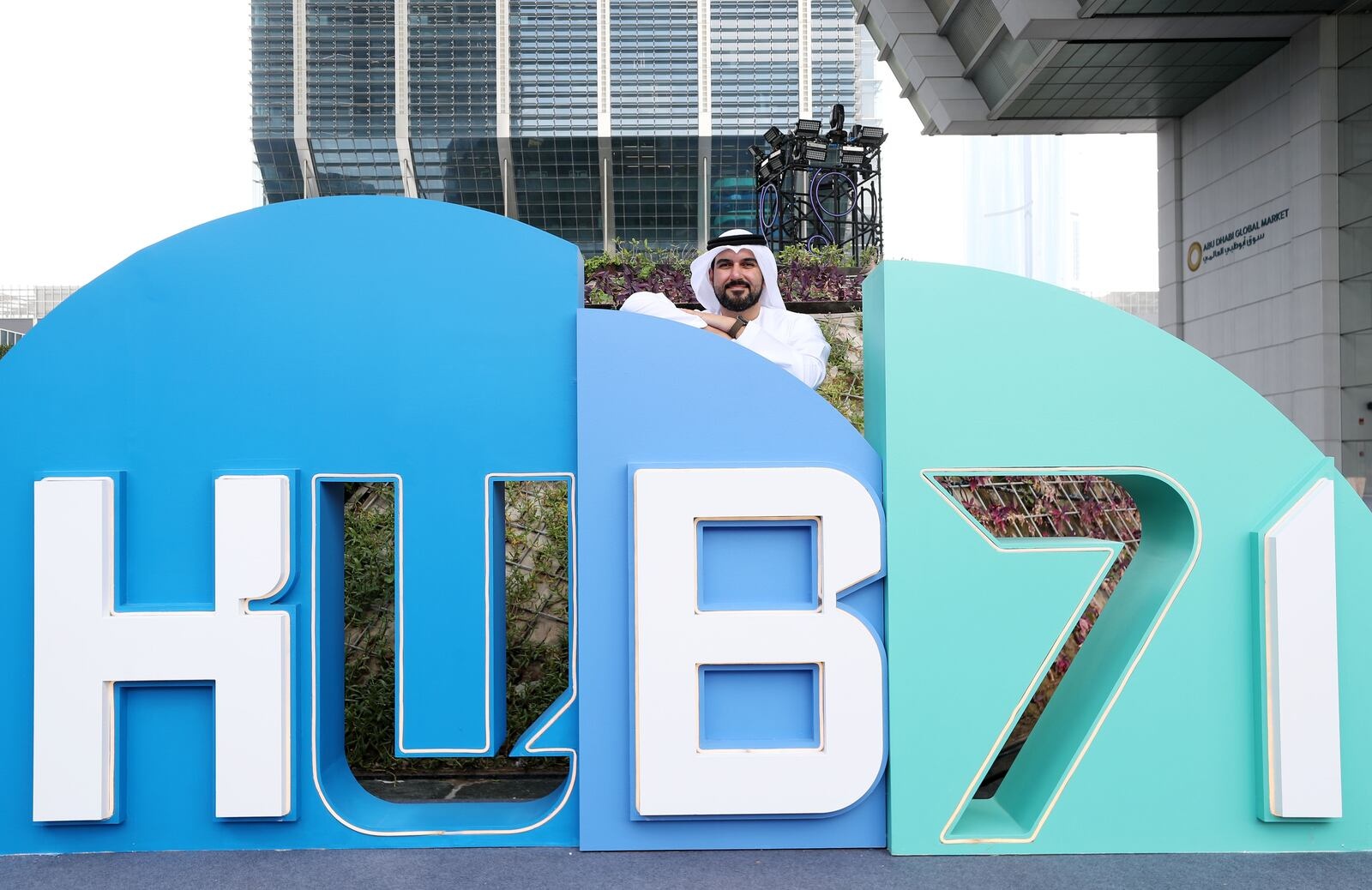 Ahmad Ali Alwan standing behind the large blue and turquoise Hub71 sign in Abu Dhabi