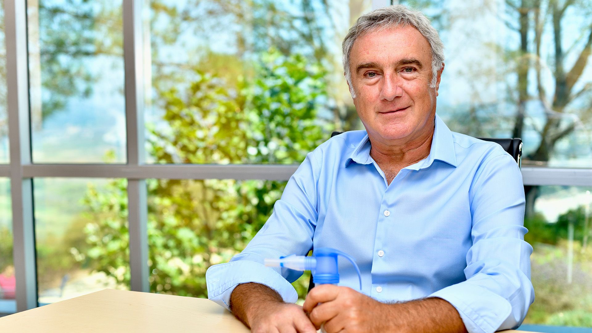 Ahmet Tutuncu seated at a table holding a blue nebulizer component