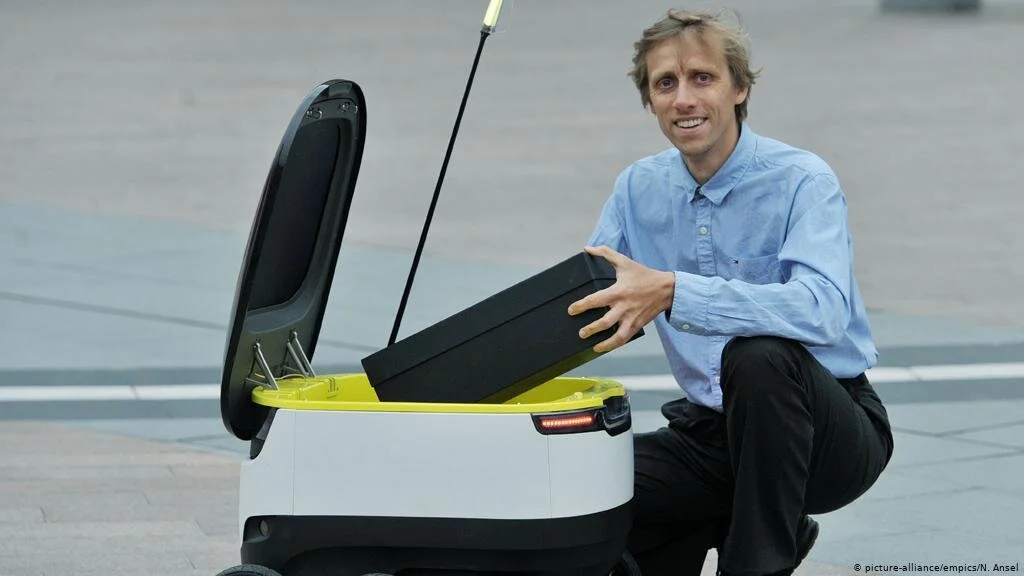 Ahti Heinla crouches beside an open Starship robot, lifting its cargo insert.