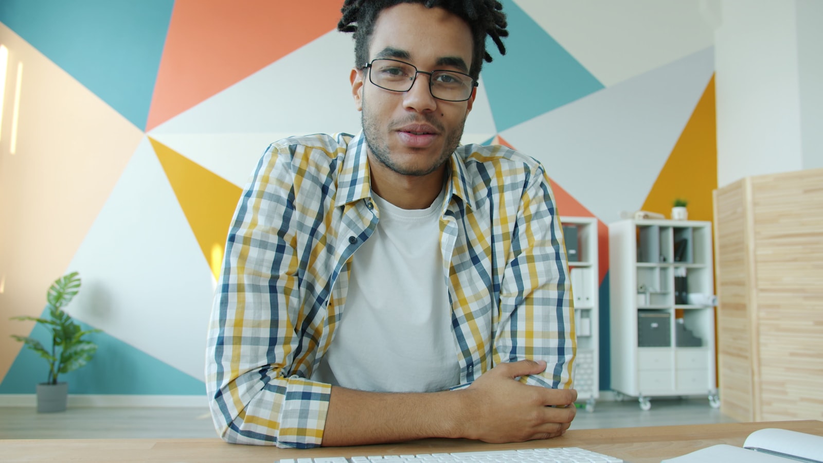 A person on a video call from a home office, gesturing at the camera