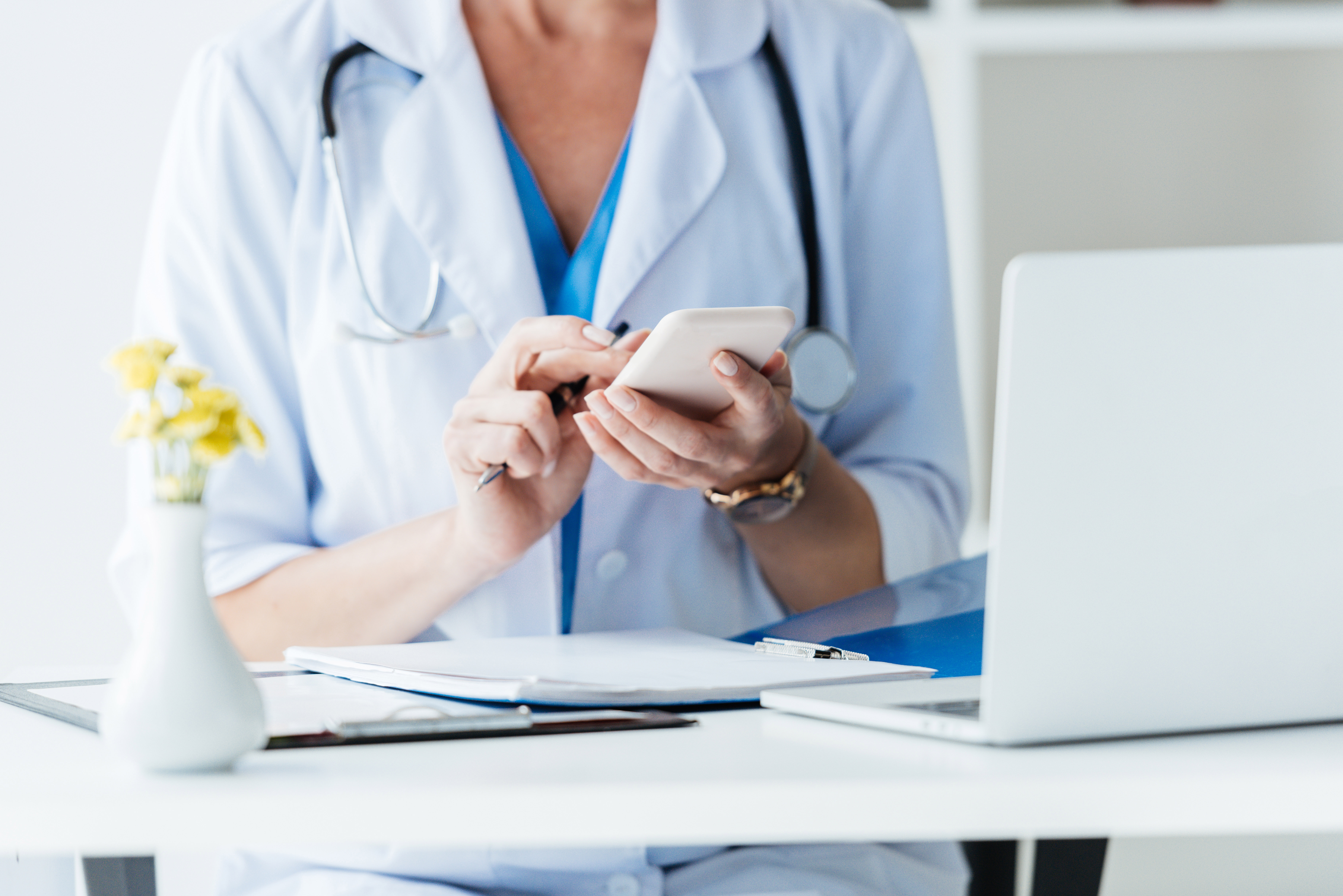 Healthcare marketing photograph from Aim’s archived website showing a clinician using a smartphone beside a laptop.