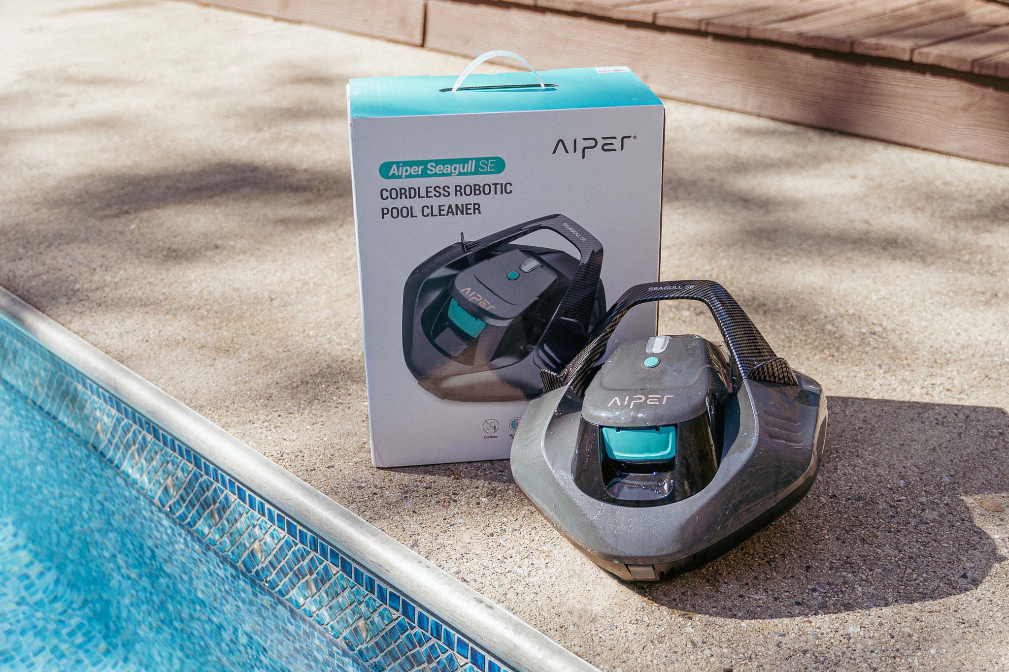 Aiper Seagull SE cordless robotic pool cleaner beside its retail box at the edge of a swimming pool
