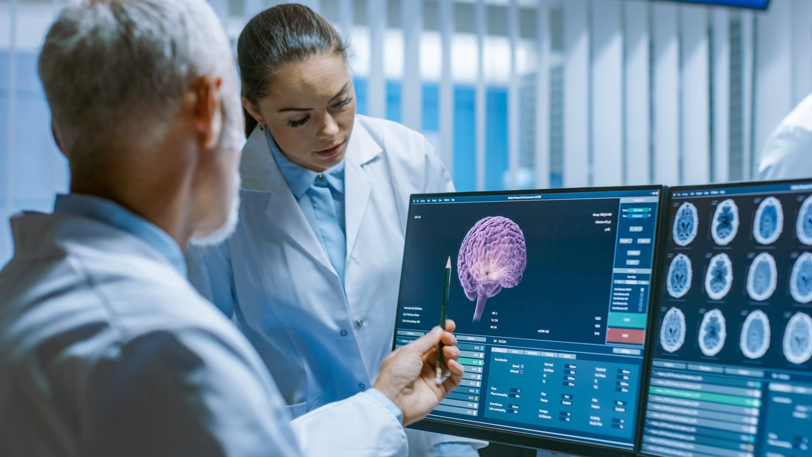 Two healthcare professionals examine brain imaging on computer monitors