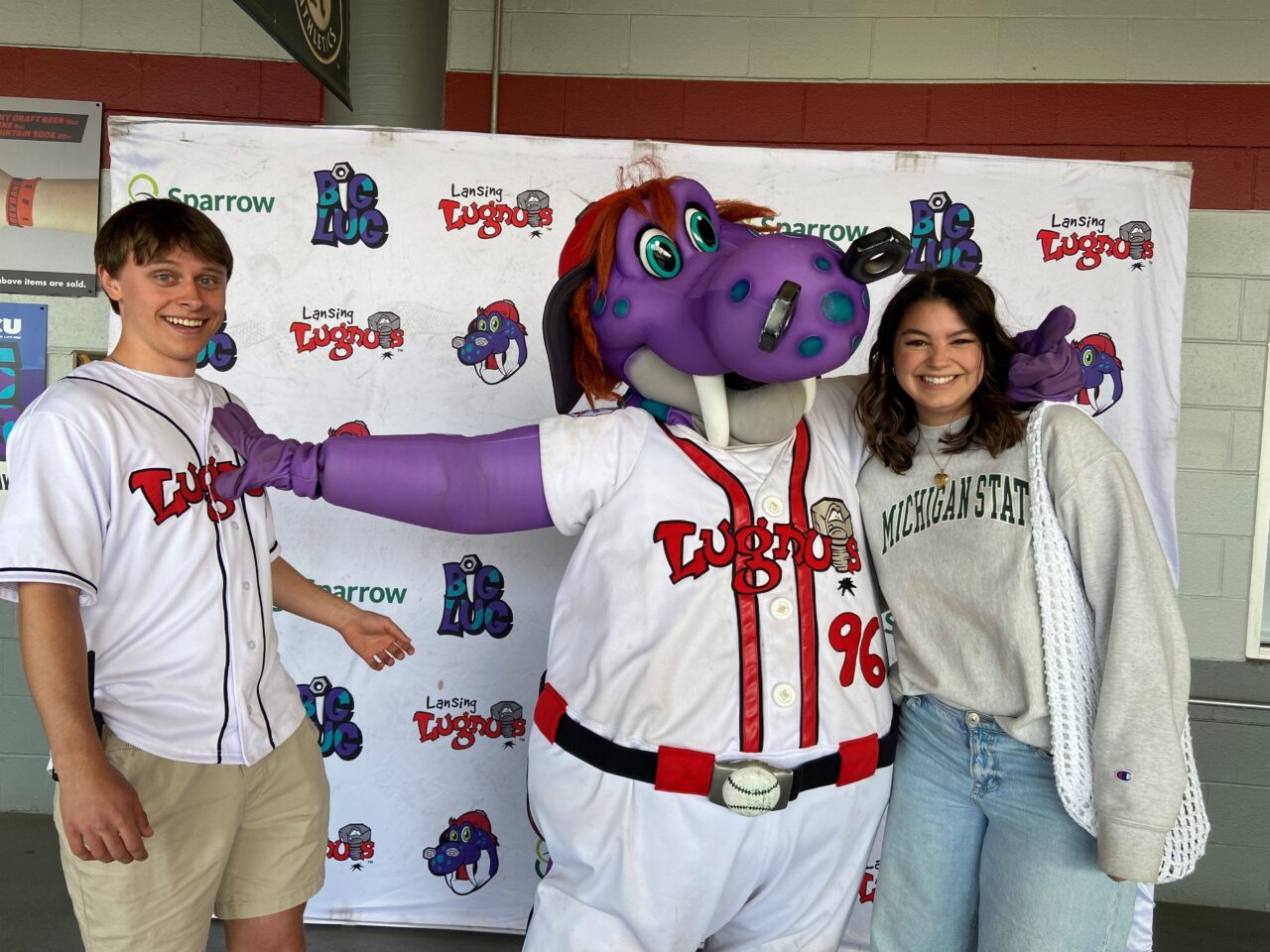 Two young people posing with the Lansing Lugnuts mascot at a community event