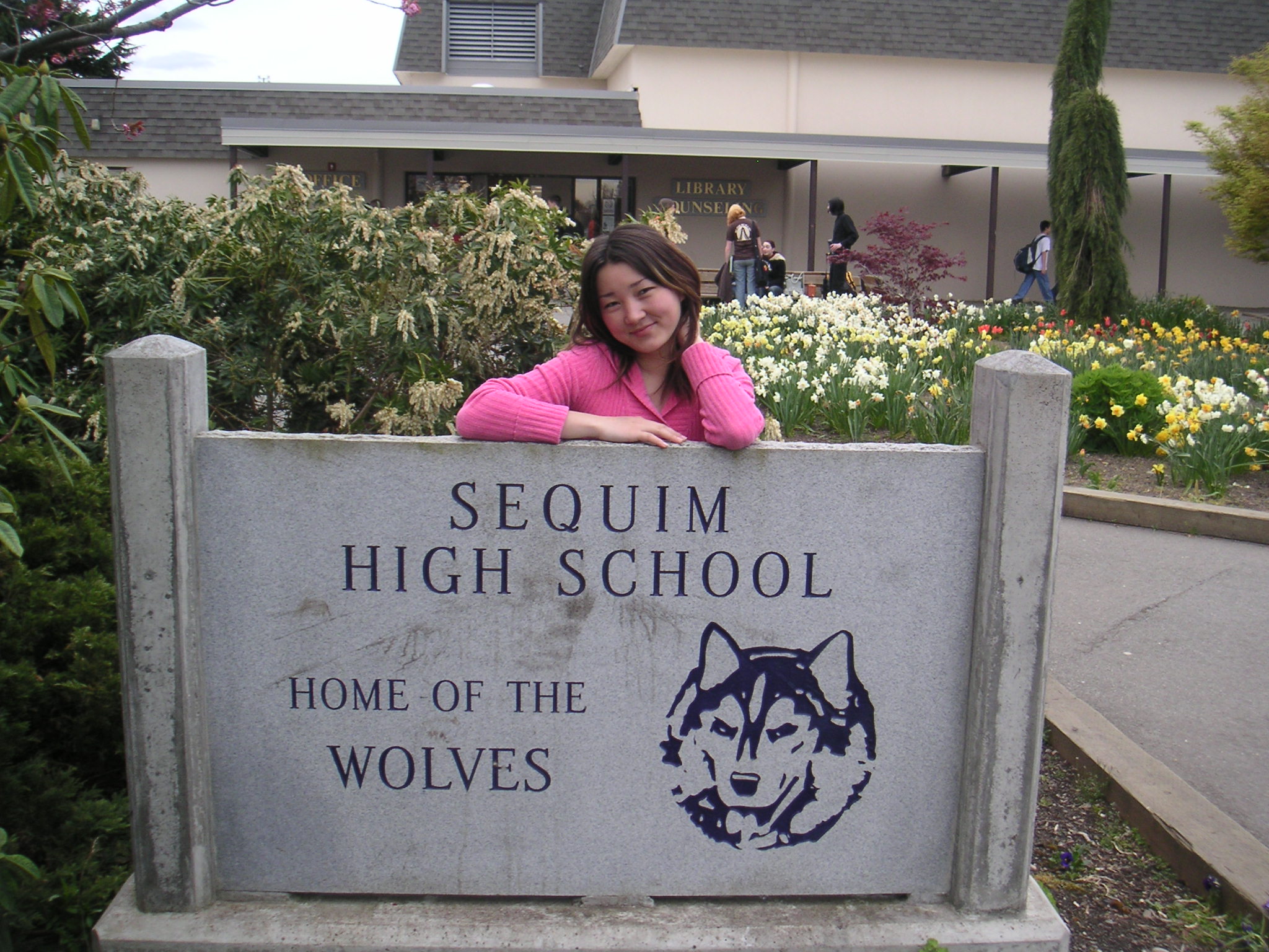 Aizada Marat in a pink sweater beside the Sequim High School sign