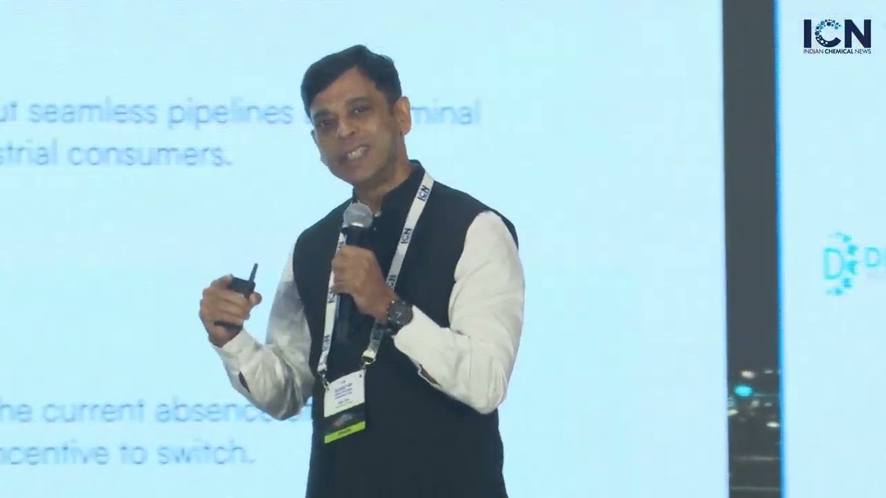 Ajay Das speaking with a microphone and presentation remote at a chemical industry conference