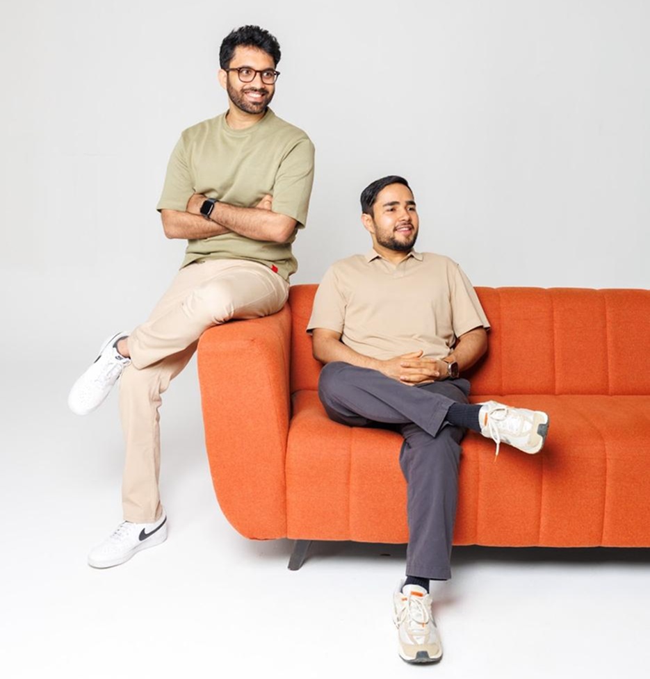 Arjun S sits on the left arm of an orange sofa beside Akshat Tyagi, seated at right