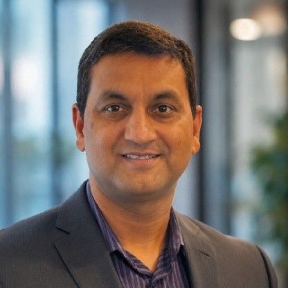 Akshay Jain wearing a dark jacket and open-collar shirt in an indoor setting