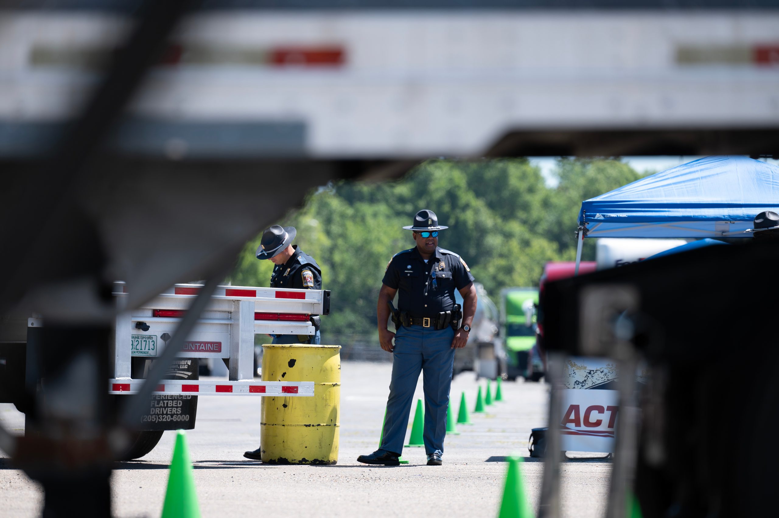 Two uniformed officials stand among trucks and traffic cones during an Alabama trucking skills event