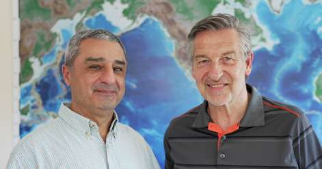 Bijan Mohammadi, left, and Alain Fanet, right, standing together before a world map