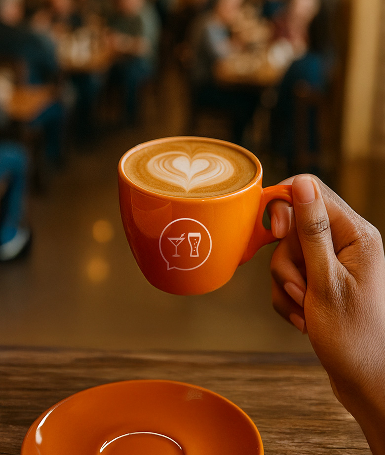 An orange SpotHopper coffee cup with latte art in a café setting