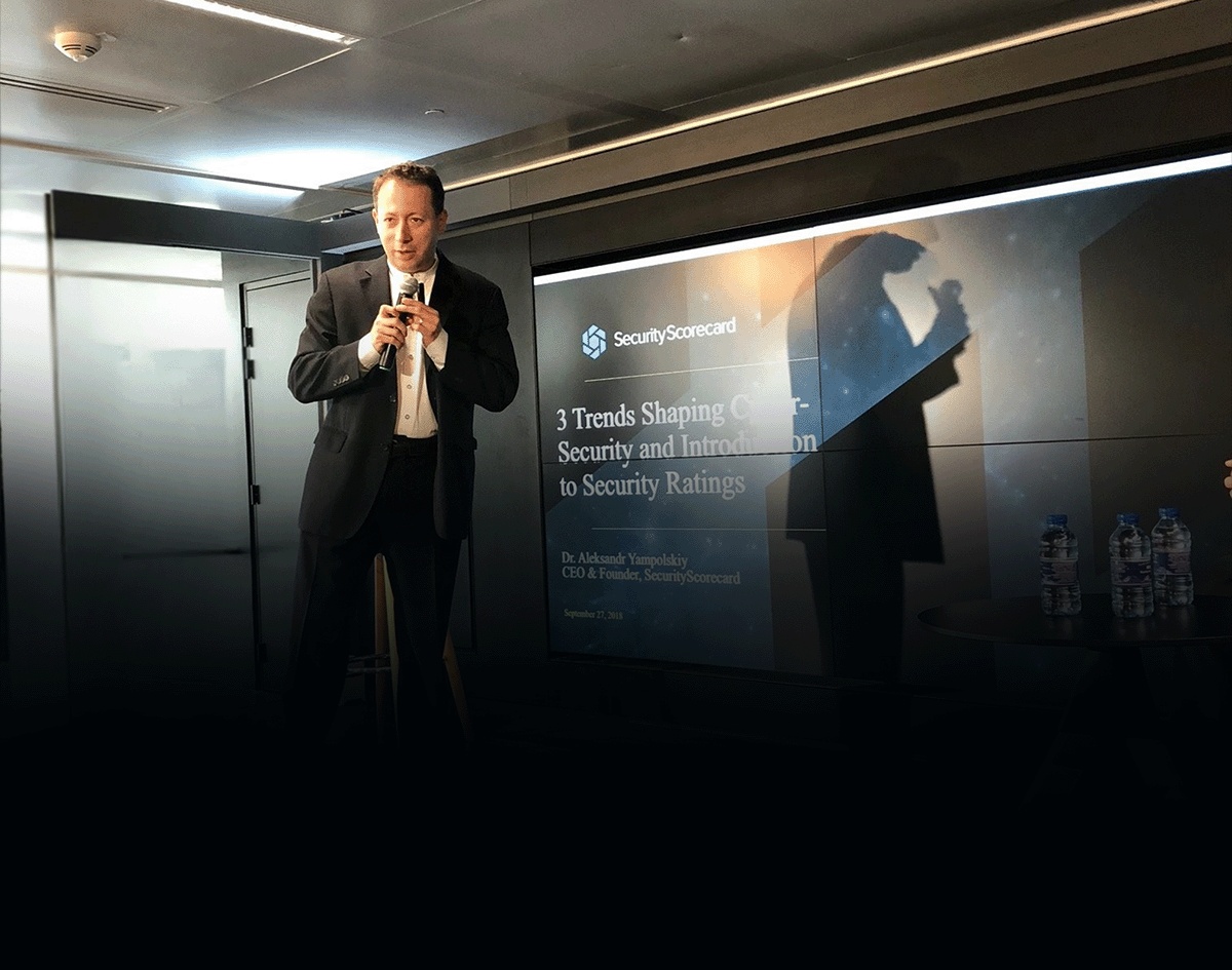 Aleksandr Yampolskiy holding a microphone beside a SecurityScorecard presentation