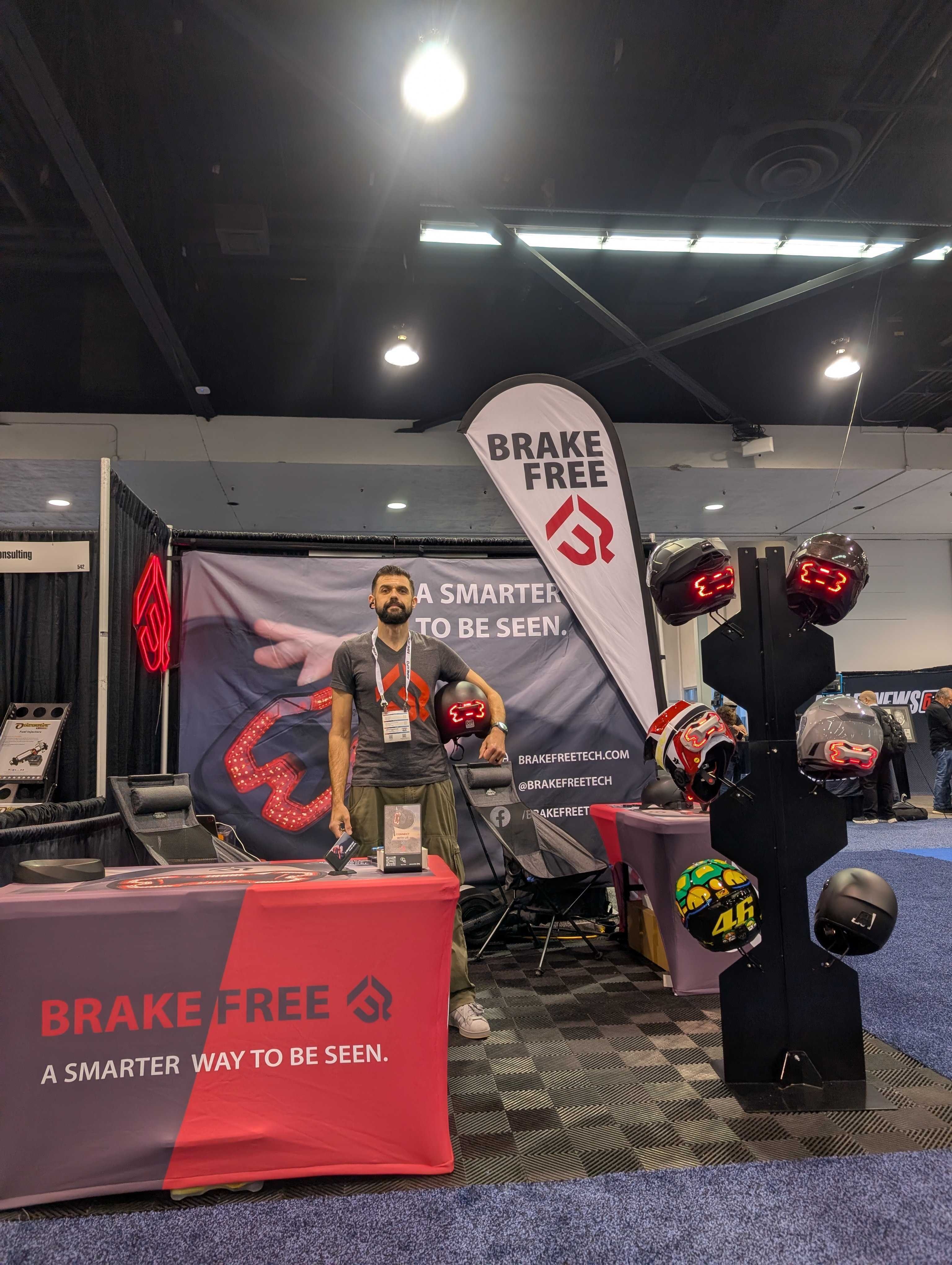 Alex Arkhangelskiy at the Brake Free booth at AIMExpo 2026, beside a display of illuminated motorcycle helmets