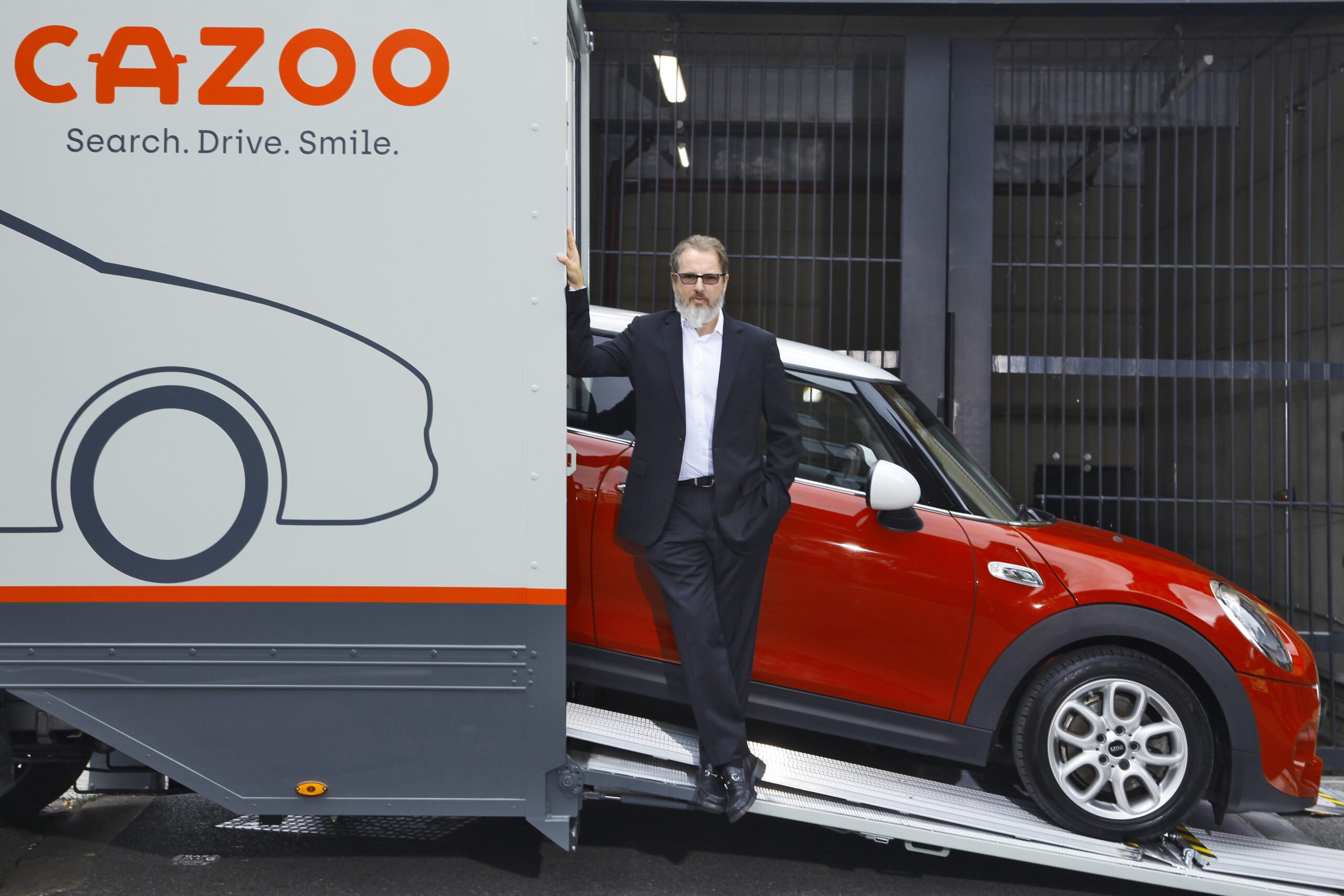 Alex Chesterman standing on a Cazoo transporter beside a red Mini