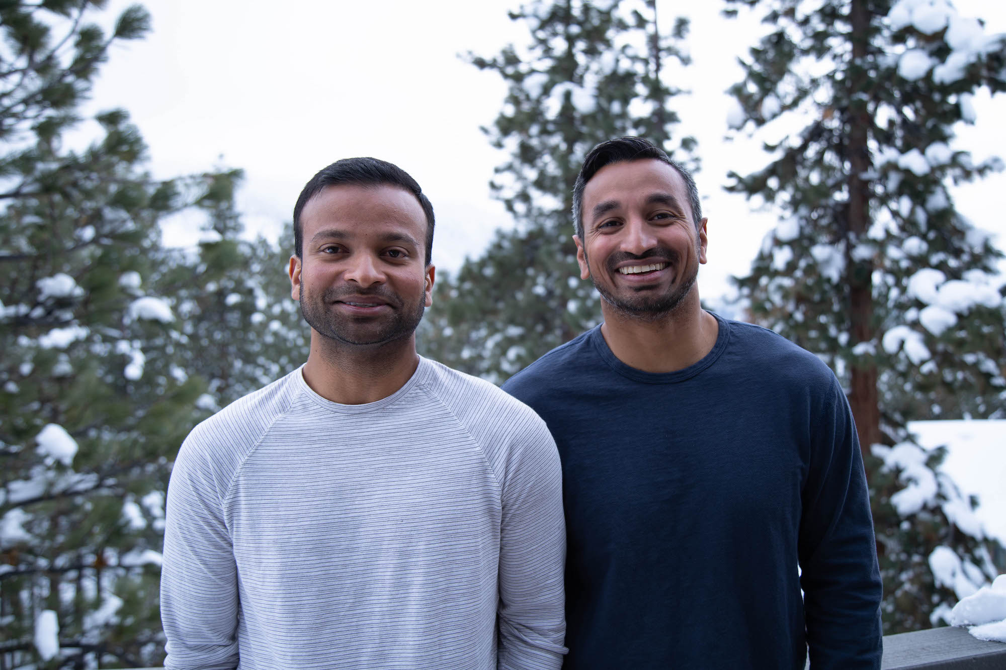 Alex Cyriac, left, and Shobin Uralil stand together outdoors among snow-covered trees.