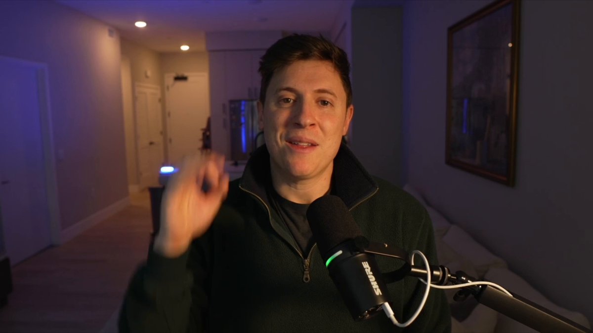 Alex Finn speaking to camera beside a microphone in his home recording space