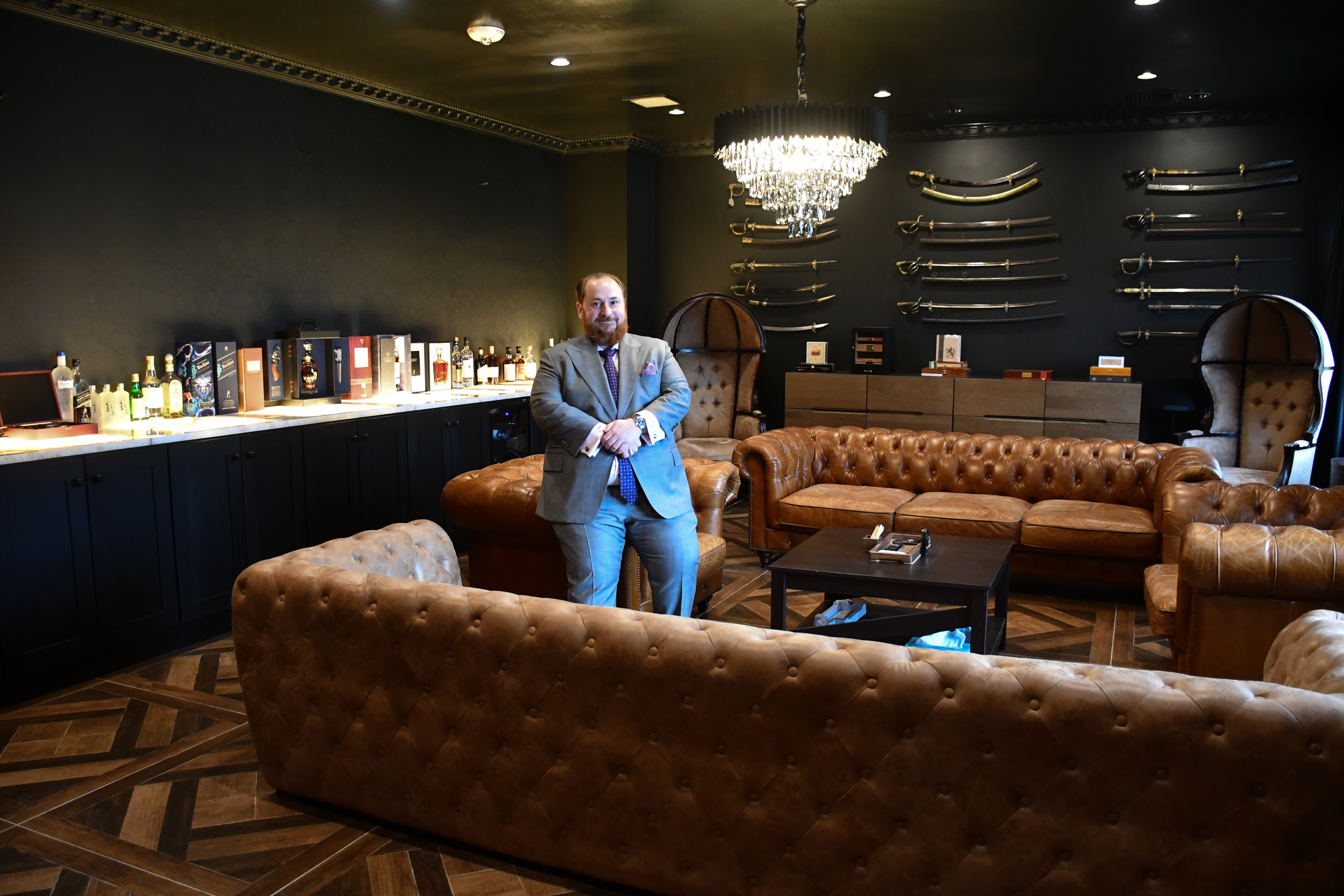 Alex Groyzburg in a lounge furnished with leather sofas and a display of swords