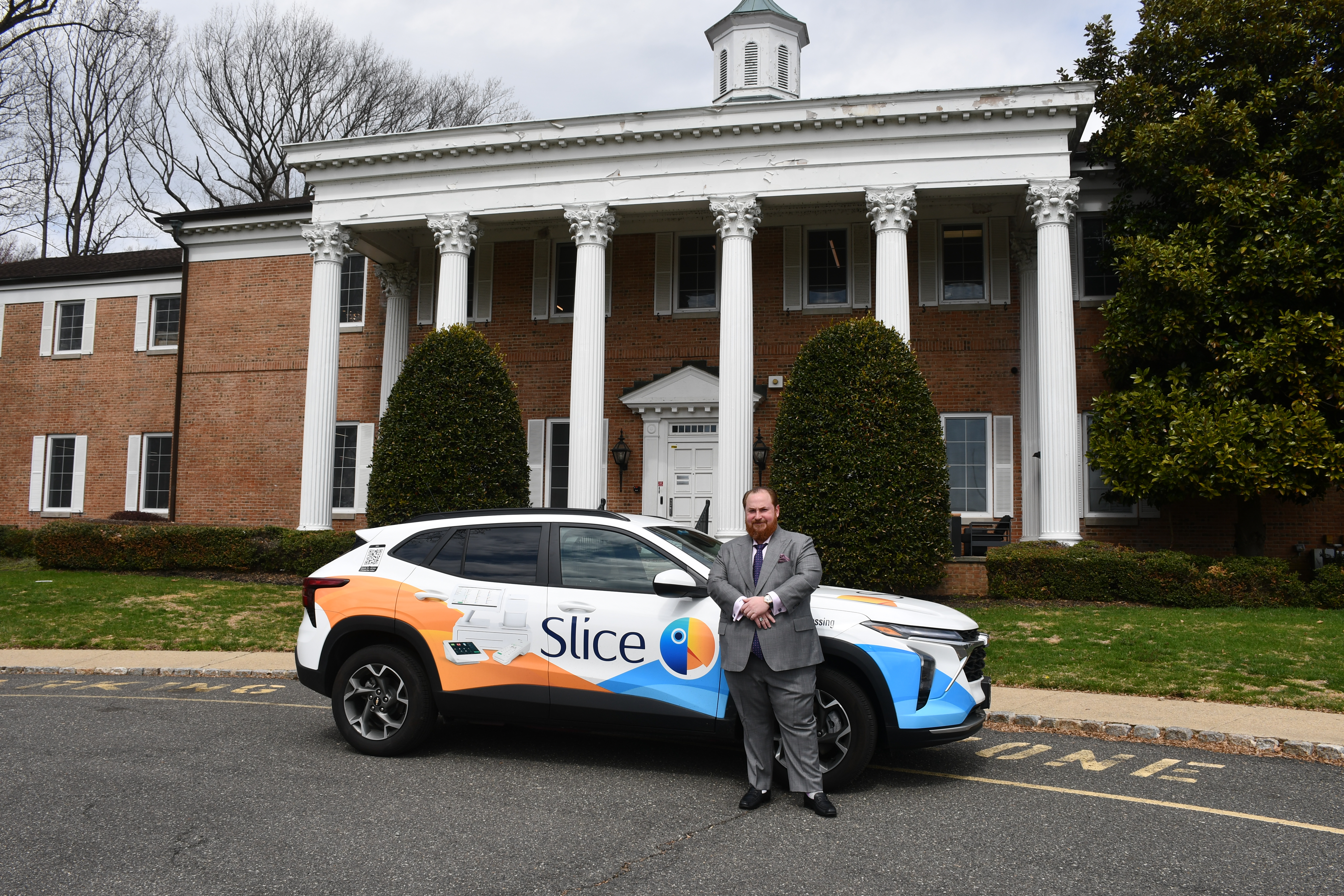 Alex Groyzburg standing beside a Slice-branded vehicle outside a brick building