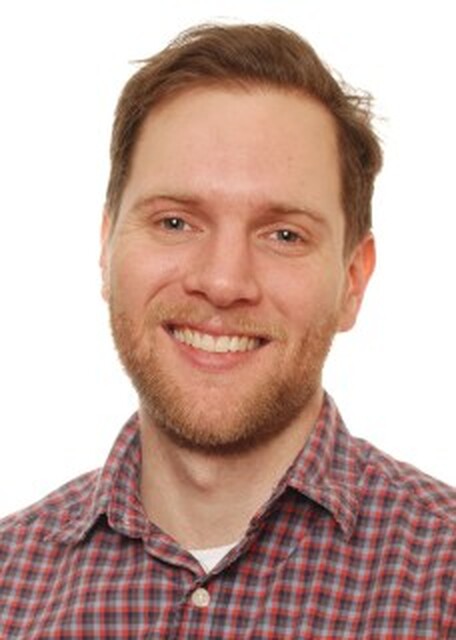 An earlier portrait of Alex Hayter smiling in a plaid shirt