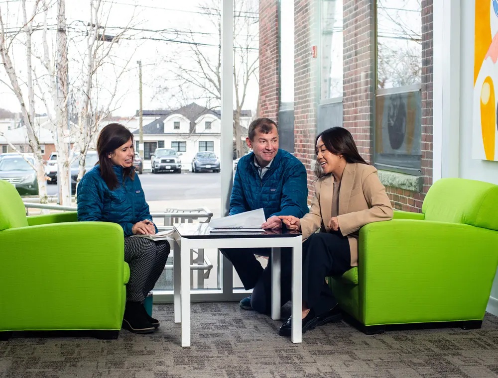 Three Diagonal colleagues discussing documents around a low table in a bright office.