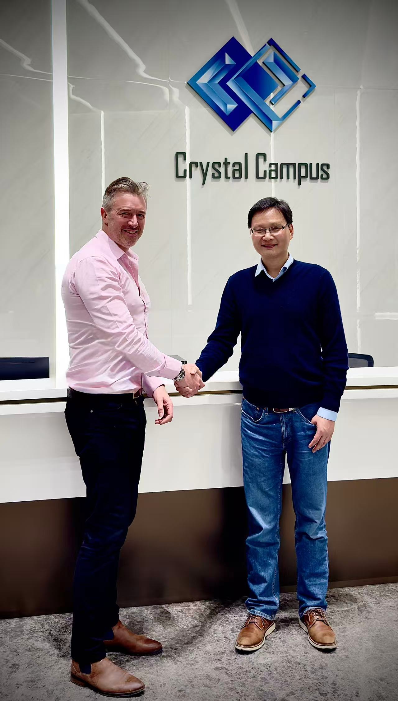 Alex Chen, on the right, shaking hands with a collaborator beneath the Crystal Campus sign