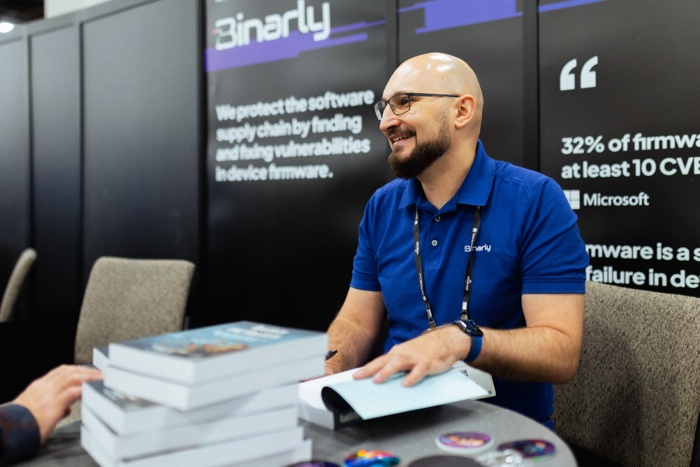 Alex Matrosov smiling at a Binarly booth with copies of his book on the table