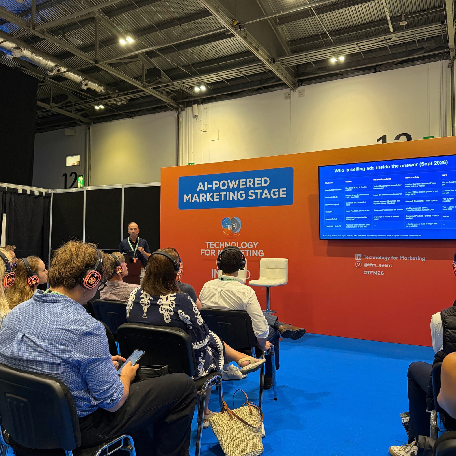 Alex Melen speaking to an audience wearing headphones at the AI-powered marketing stage in London