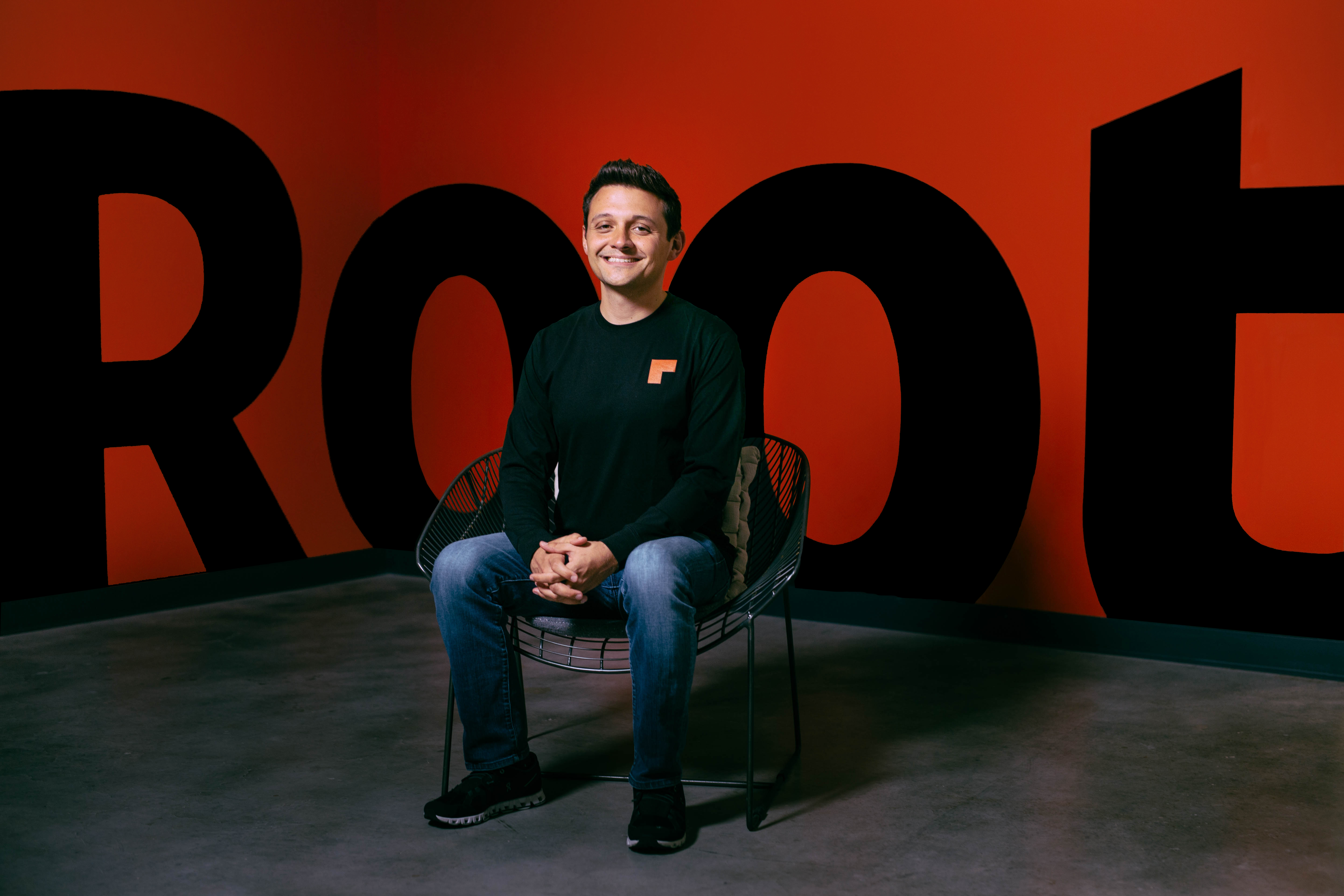 Alex Timm seated in a chair in front of an orange Root wall