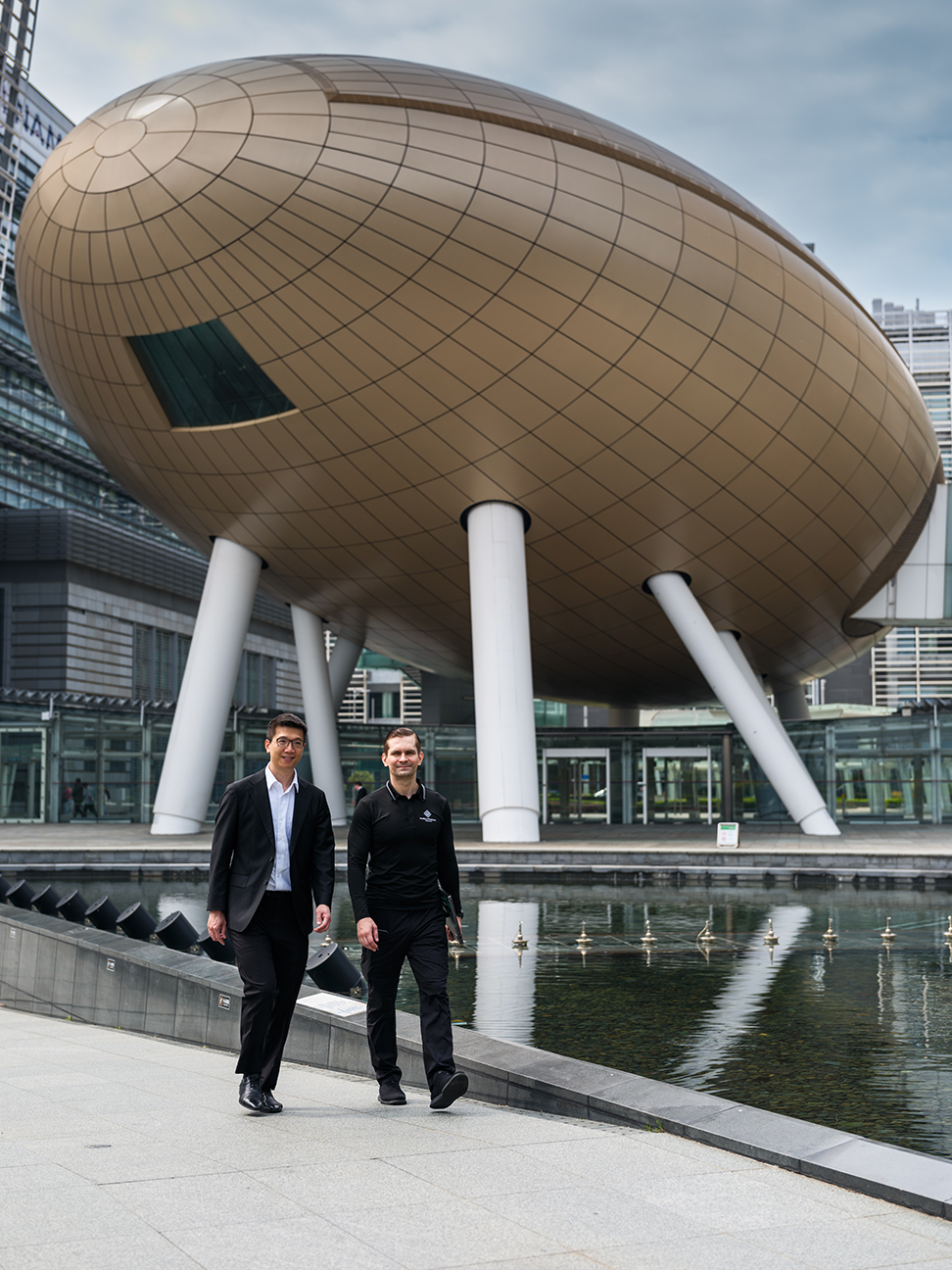 Jeremy Lui and Alex Zhavoronkov walking beside a reflecting pool in Hong Kong