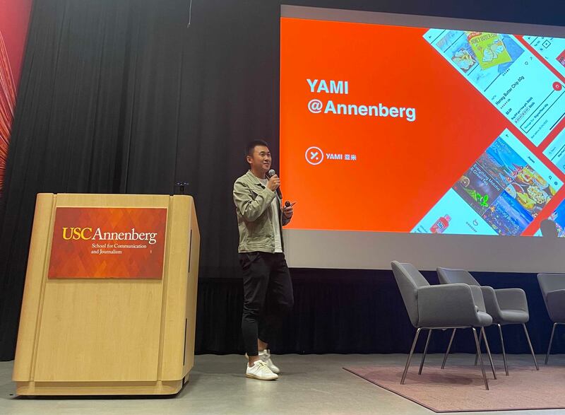 Alex Zhou speaking with a microphone at USC Annenberg beside a Yami presentation