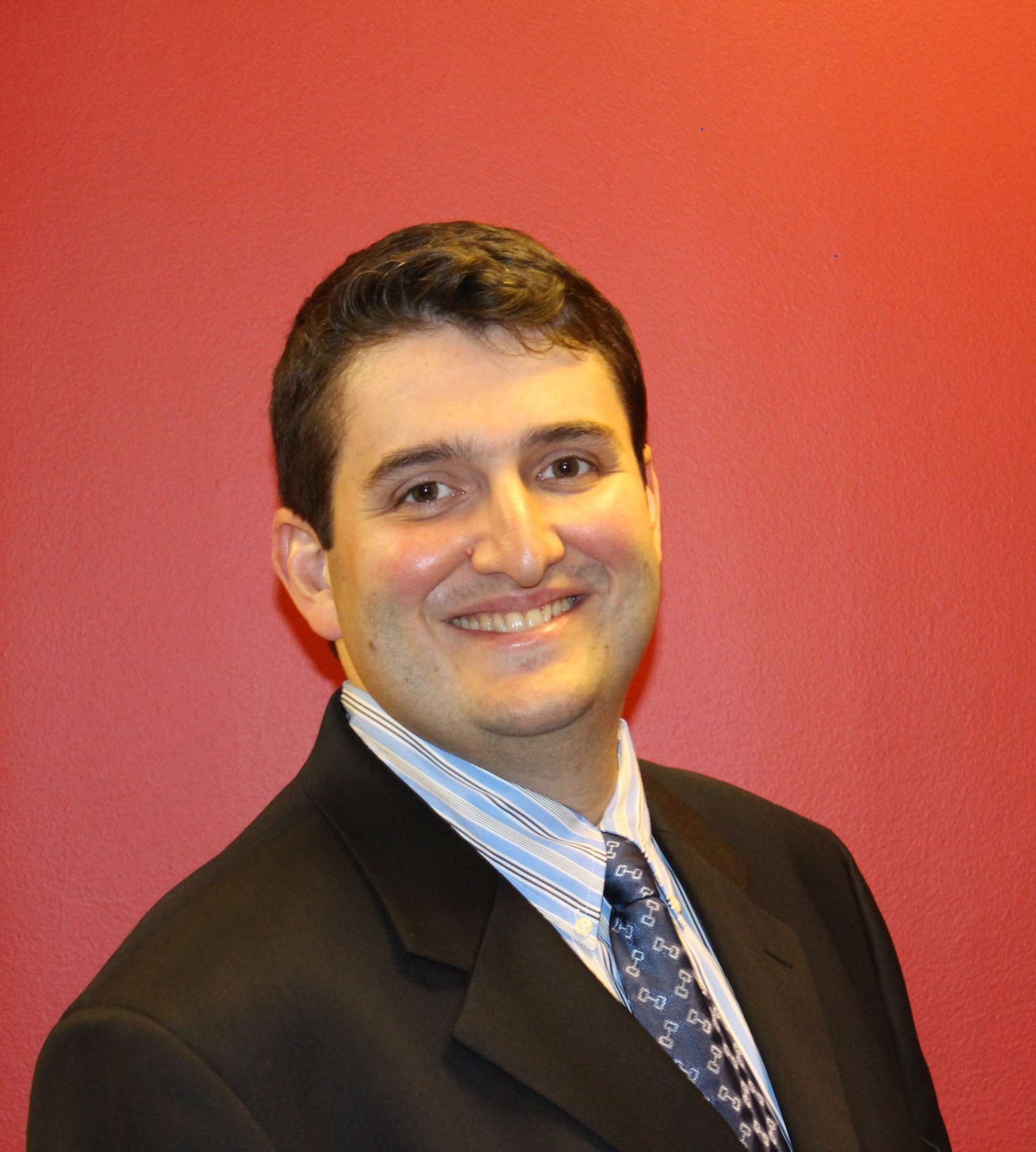 Alexander Kesler in a suit and patterned tie against a red wall, in an archival photograph published with his 2018 interview