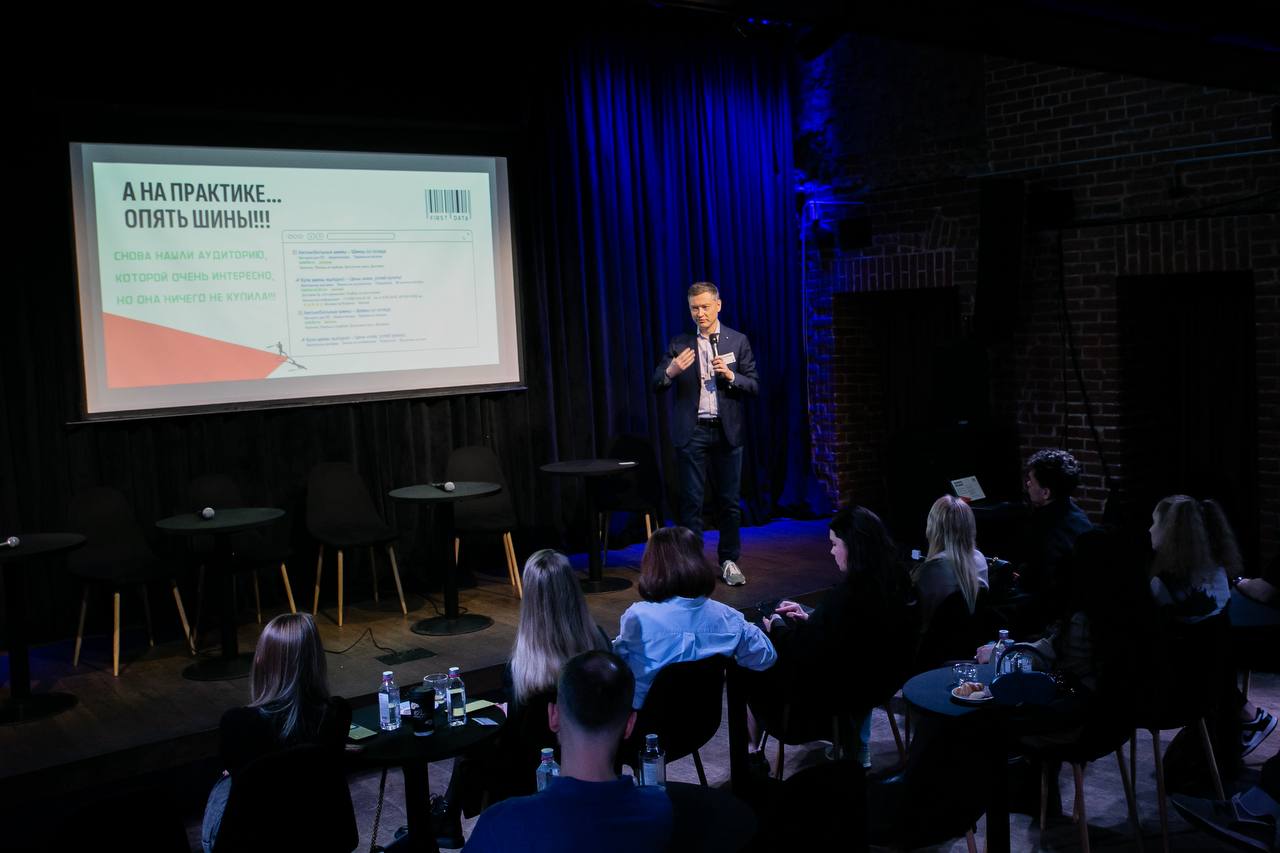 Alexander Starostin speaking beside a presentation screen to a seated conference audience