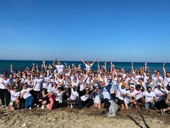 Nfinite colleagues gathered on a beach in matching white shirts