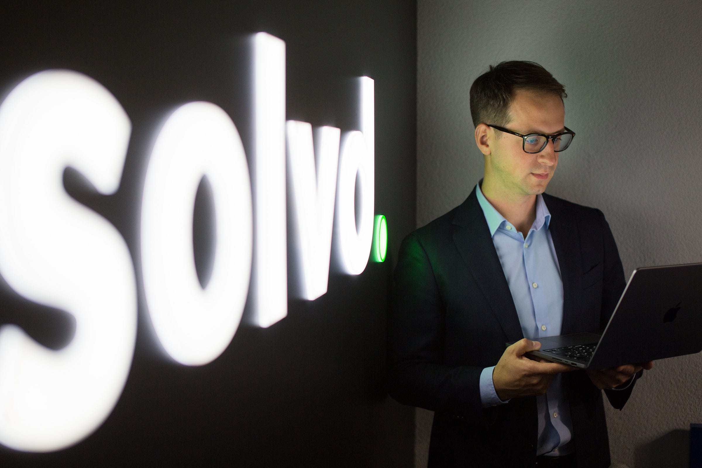 Alexey Khursevich holding an open laptop beside illuminated Solvd lettering