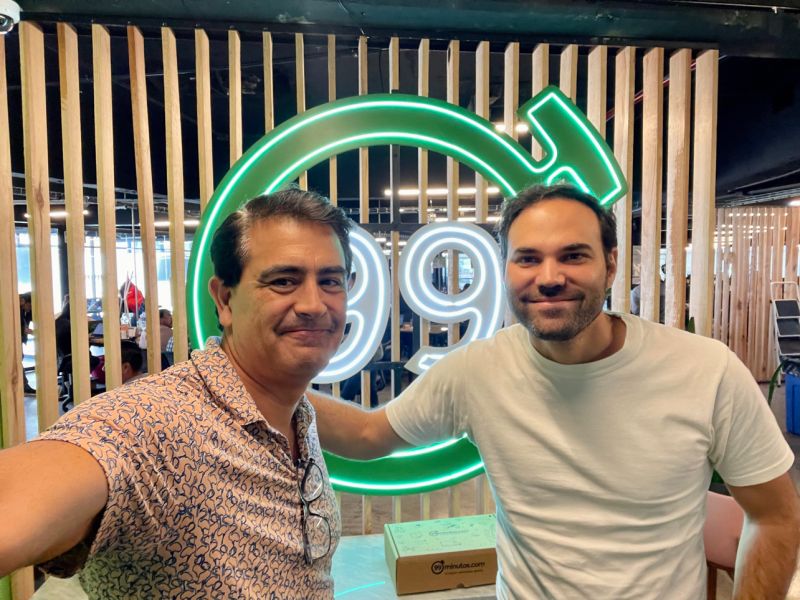 Investor Ivan Montoya, left, and Alexis Patjane, right, in the 99minutos office beside a glowing 99 sign.