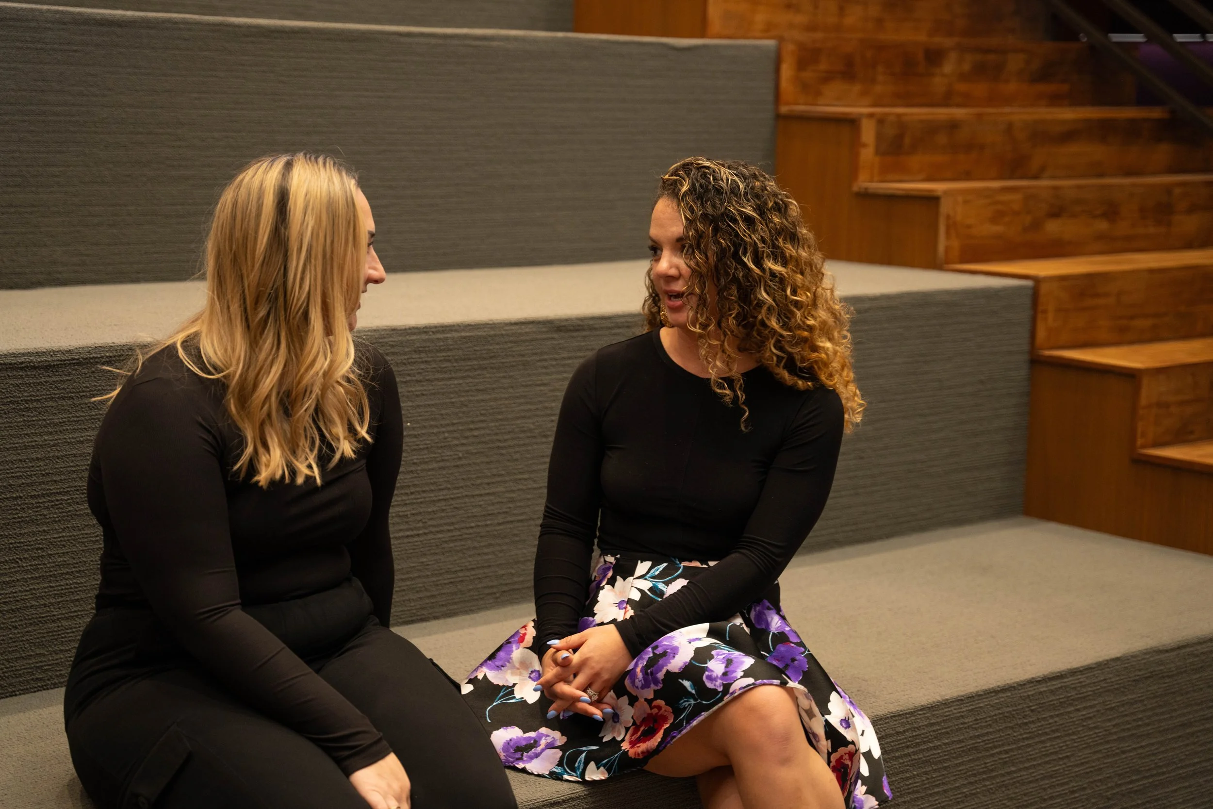 Alexis Quintal, right, talking with another woman while seated on tiered steps