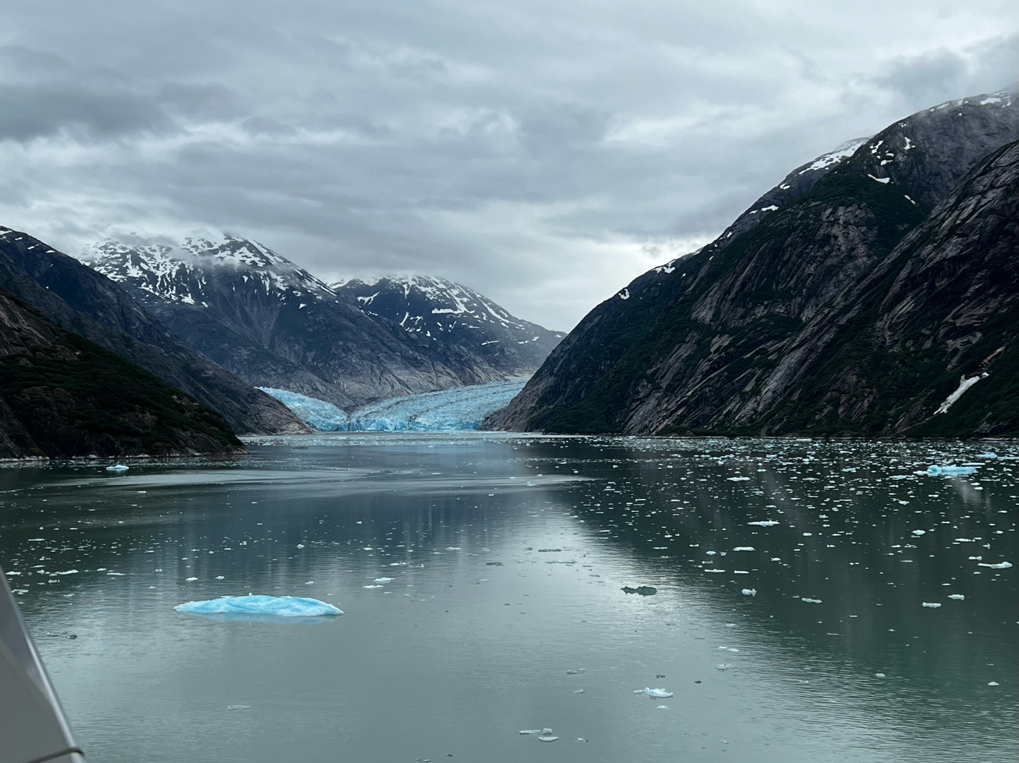 A blue glacier between dark mountains in an Alaskan fjord