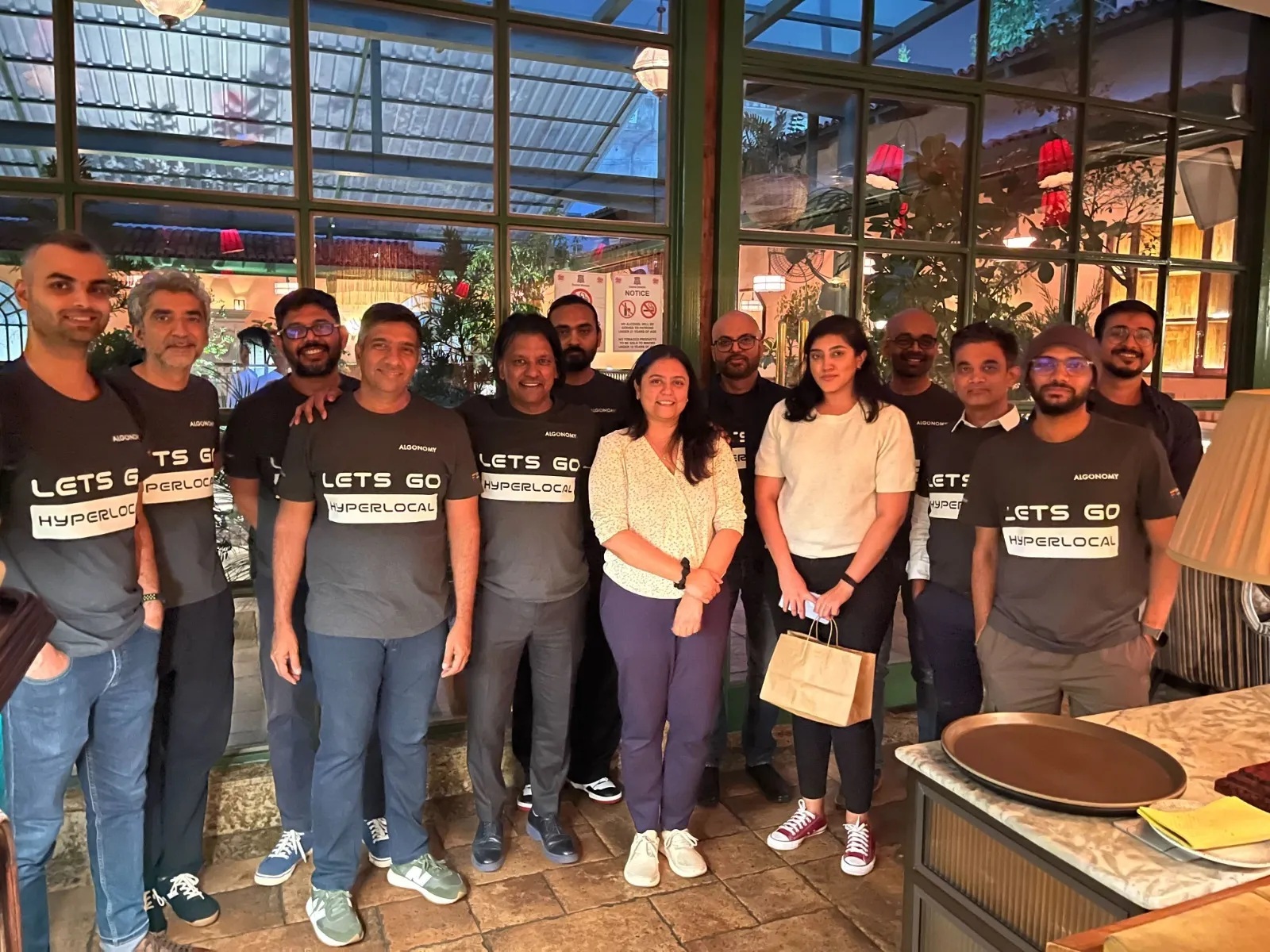 Algonomy team members gathered indoors, several wearing Let’s Go Hyperlocal shirts